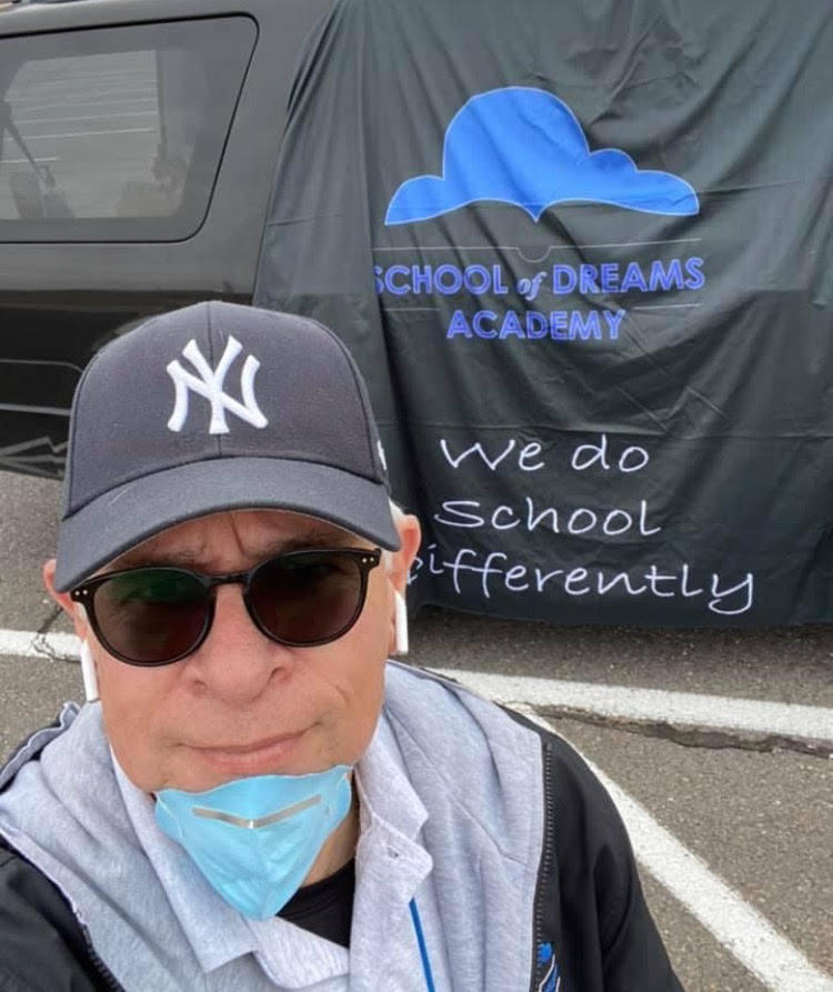 Superintendent Mike Ogas standing in front of a School of Dreams Academy banner that reads "We Do School Differently" while delivering lunches during the pandemic. 